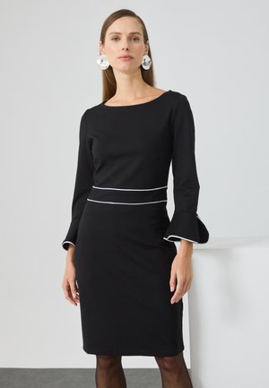 Abito nero con maniche lunghe, polsini svasati e rifiniture bianche in vita. Tessuto liscio, design al ginocchio, stile minimalista.