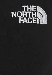 Una tela negra con una textura acanalada presenta un destacado logo bordado en blanco que dice "THE NORTH FACE", acompañado de un gráfico icónico de media cúpula.