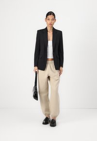 Blazer preto, top cropped branco, calças beje de cordão e mocassins pretos. Acessórios incluem uma pequena mala preta. Design simples e ajustado.