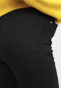 Černé džíny z denimu s přiléhavým střihem, které se vyznačují charakteristickým tvarem zadní kapsy a minimálními kovovými prvky. Měkká textura a jednobarevný design.