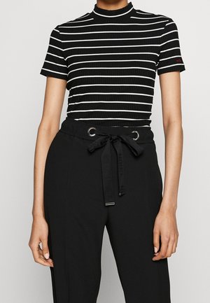 Schwarz-weiß gestreiftes, geripptes T-Shirt mit hohem Kragen; kombiniert mit hochtaillierter schwarzer Hose mit Kordelzug und Metallösen.