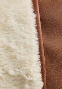Tessuto in pelliccia artificiale con un lato bianco crema accostato a una superficie marrone ricco e morbido, con un bordo liscio.