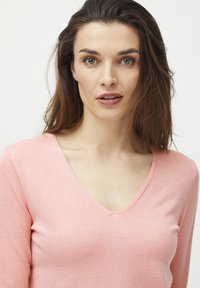 Pull à col V en tissu rose doux. Manches longues, design ajusté avec des détails de couture subtils le long de l'encolure et de l'ourlet. Texture uniforme.
