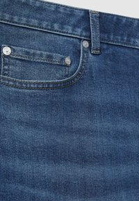 Tamno plave traperice s prednjim džepom, srebrnim detaljima, suptilnom teksturom i kontrastnim šavovima.