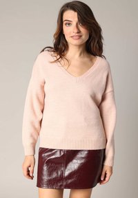 Pull à col en V rose pâle avec des poignets et un ourlet côtelés, associé à une mini-jupe en simili cuir bordeaux brillant. Les deux vêtements ont des textures douces.