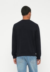 Svart hettegenser med lange ermer, rund hals og ribbestrikkede mansjetter. Stoffet ser glatt og mykt ut. Brukt med lyseblå jeans.