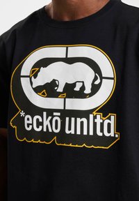 Juodas medvilninis marškinėliai su išryškinta balta rhino grafika, apibendrinta rėmelyje, akcentuota geltonais ir ryškiais užrašais "eckō unltd."