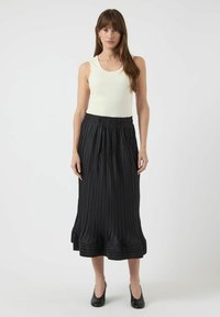 Sort plisseret midi-nederdel med elastisk talje, kombineret med en tætsiddende cremefarvet tanktop. Modellen har sorte hæle på. Glat tekstur, lagdelt kant.