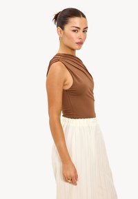 Bruine mouwloze bodysuit met gedrapeerde halslijn, gecombineerd met een witte geplisseerde rok. Gladde stof met subtiele glans, recht silhouet.