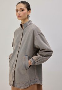 Svetlo siva denim jakna z ovratnikom, zapiranjem na gumbe, elastičnimi manšetami in stranskimi žepi. Ima sproščen kroj in subtilno bledenje.