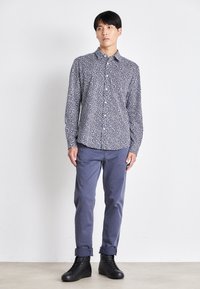 Camisa con un estampado floral en azul marino y blanco, diseño de botones, combinada con pantalones ligeros azul claro arremangados y botas negras de cordones.