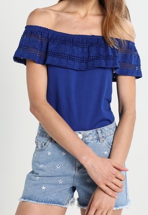 Haut bleu marine à épaules dénudées avec des détails en dentelle et un bord à volants, associé à un short en denim bleu clair orné de fleurs brodées.