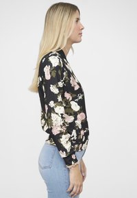 Blusa floreale con sfondo nero e grandi fiori rosa e bianchi, maniche arricciate e vestibilità rilassata. Il materiale sembra leggero.