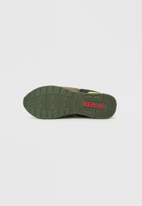 Sola de borracha verde com padrões de pega, apresentando acentos em amarelo e preto. Logotipo vermelho "REPLAY" na lateral. Material superior em camurça e tecido.