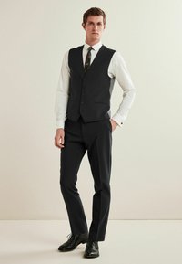 Herren maßgeschneiderter dunkelgrauer Anzug mit einer Sechs-Knopf-Weste, weißem Hemd, gemustertem Schlips und schwarzen eleganten Schuhen. Glatte Stoffoberfläche.