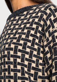 Pull en maille avec un motif géométrique en noir et beige, doté d'un col côtelé et d'une surface texturée pour plus de chaleur.