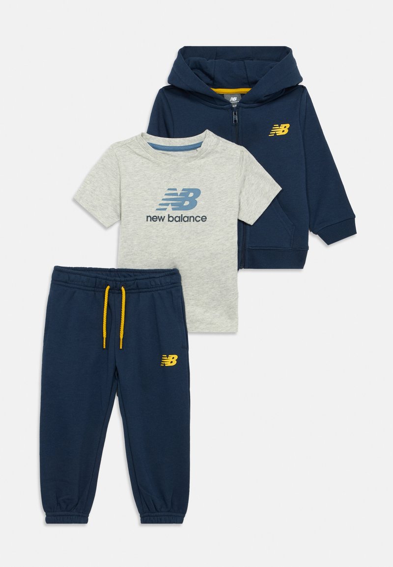 Lille barns navy blå zip-up hoodie, matchende joggingbukser med gule snore og lysegrå New Balance t-shirt med kortærmer og logo.