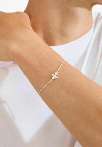 Zilveren armband met een fijne ketting, met in het midden een klein kruisje als ontwerp. De zichtbare huidtint is licht.