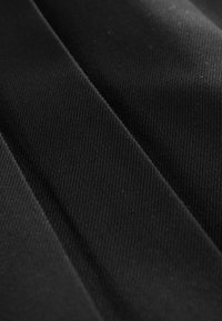 Tissu noir avec un tissage texturé et côtelé, présentant des plis horizontaux et des variations de surface lisses.
