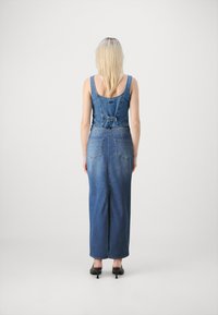 Denim kombinezon z oprijetim zgornjim delom, nastavljivimi naramnicami in pasom. Oblikovanje do gležnjev ima gladko, klasično modro površino.