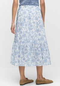 Blommig midi kjol i vitt med blått mönster, med ett lager-på-lager design och elastisk midja. Matchad med bruna slip-on skor.