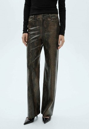 Woman wearing high-waisted, wide-leg faux snakeskin leather pants with pointed black heels and a black long-sleeve top against a white background.
