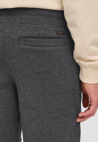 Pantalons de survêtement gris avec une texture douce, dotés d'une poche arrière et d'un petit label de marque. La ceinture présente un design côtelé.