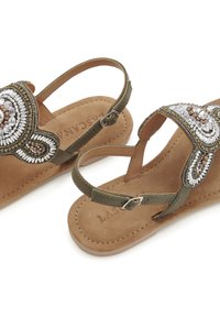 Beaded sandal with an olive green strap, intricate embroidery, and a soft suede insole. Features an adjustable ankle strap and decorative accents.