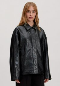 Zwarte faux leren jack met een kraagontwerp, oversized pasvorm en zichtbare naaddetails. Heeft zijzakken en een soepele textuur.