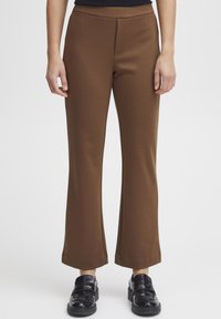 Pantalons bruns ajustés avec une jambe droite et une texture subtile. Ils présentent une taille moyenne et sont associés à des chaussures noires.