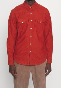 Rood corduroy overhemd met een puntige kraag, drukknopen, twee borstzakken en een afgeronde zoom. Gladde textuur en Western-stijl schouderstukken.