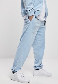 Light blue jogger pants made of soft fabric with a subtle pattern, featuring side pockets and elastic cuffs, paired with white sneakers.