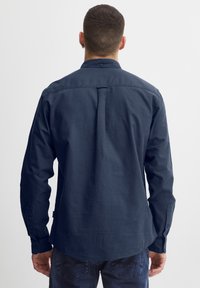 Marineblå langermet skjorte med krage med knapper, bakfold detalj og knappedeler, laget av glatt, lett stoff.