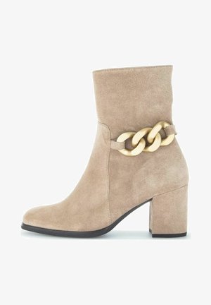 Stivale alla caviglia in suede beige con tacco chunky. Presenta un accento in catena dorata sul lato, cuciture senza soluzione di continuità e una punta arrotondata.