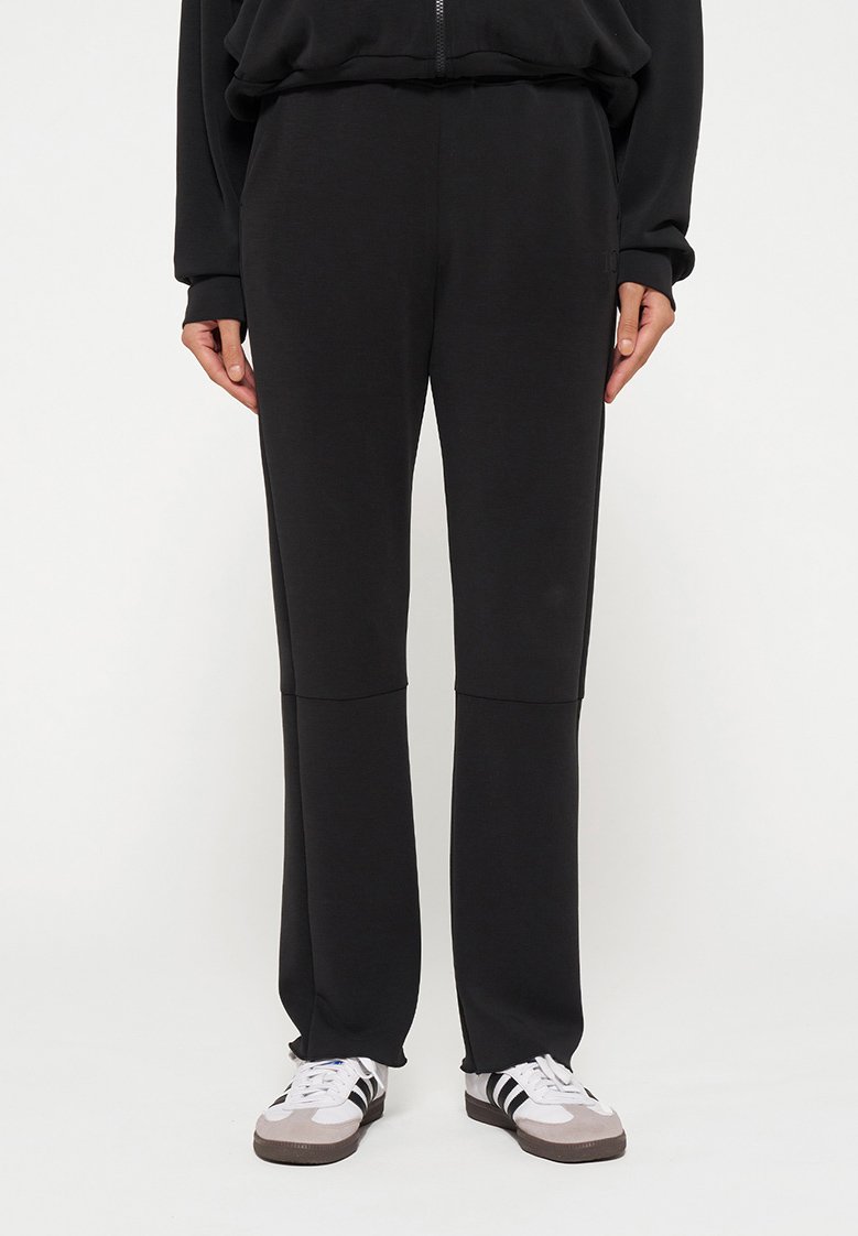 Black sweatpants made from soft fabric, featuring a relaxed fit, and a paneled design with a smooth texture. Paired with white and gray sneakers.