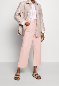 Light beige glossy jacket over a striped pink and white shirt, paired with loose pink jeans and tan sandals with buckles.