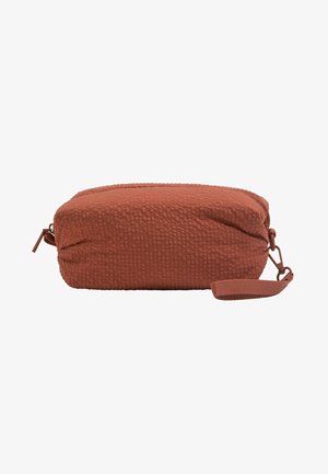 Pochette rectangulaire en tissu texturé couleur rouille avec fermeture zippée et sangle de poignet attachée sur fond blanc.