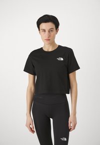 Black cropped t-shirt with short sleeves, made of cotton, featuring a small white logo on the left chest area. Paired with black leggings.