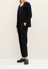 Námořnický blazer a odpovídající vypasované kalhoty vyrobené z texturované tkaniny, doplněné černými mokasíny. Minimalistický design s moderní siluetou.