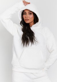 Haut à capuche en polaire blanche avec une finition douce et texturée. Dispose d'une capuche, de poignets côtelés et d'une poche avant. Doublure intérieure lisse.