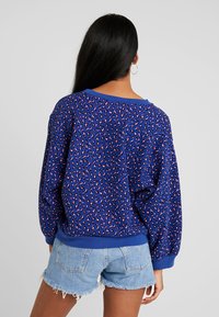 Sweat-shirt bleu avec imprimé léopard rose, coupe ample, encolure large et manches bordées; associé à un short en denim clair.