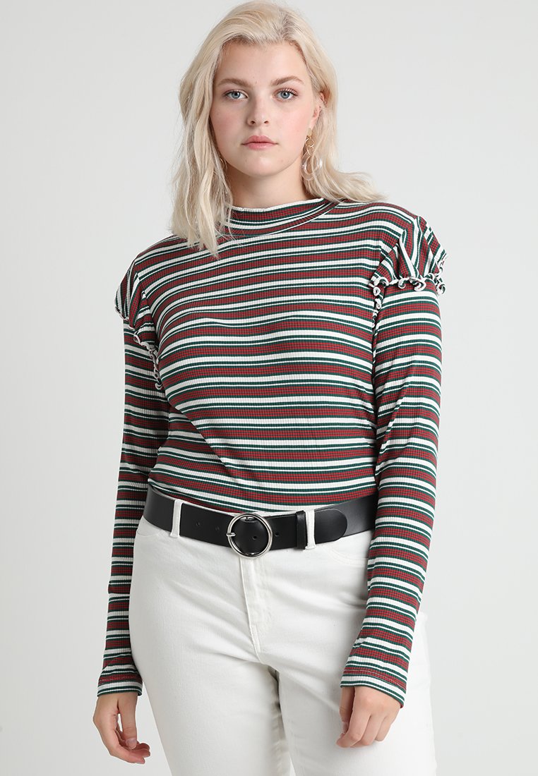 Langærmet stribet top med ribstrik i horisontale grønne, røde og hvide striber. Har flæser ved skuldrene og en rund halsudskæring, parret med højtaljede hvide bukser.