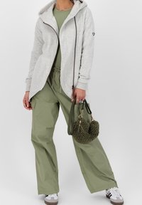 Harmaa vetoketjullinen huppari, jossa on huppu ja musta sydänlogo, yhdistettynä oliivinvihreisiin cargo-housuihin ja pörröiseen vihreään käsilaukkuun. Housuissa on taskut.