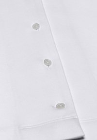 Witte katoenen shirt met een gladde textuur en een kraag. Beschikt over vijf ronde, doorzichtige knopen langs de sluiting. Schoon, eenvoudig ontwerp.