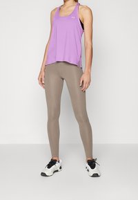 Top sportivo viola con fessure laterali, abbinato a leggings beige e sneakers bianchi e neri. Tessuto morbido e design aderente.