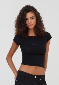 T-shirt nera cropped realizzata in tessuto morbido, con maniche corte e un piccolo logo bianco "Sweet Disaster" sul petto.