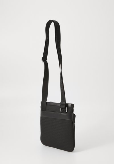Geantă crossbody neagră cu curea ajustabilă, model subtil cu logo embosat și margini din piele netedă, pe un fundal alb simplu.