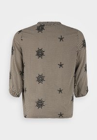 Blouse à carreaux noir et blanc avec des manches trois-quarts, ornée de motifs floraux noirs brodés dans le dos. Texture de tissu douce.