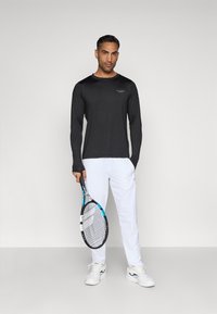 Black long-sleeve athletic shirt, white athletic pants, white sneakers, holding a black and blue tennis racket. Simple design, lightweight material.