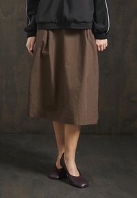 Brown knee-length skirt made of cotton material, featuring a simple design and soft texture. Paired with dark purple heeled shoes.